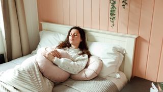 A woman lying on her bed with extra pillows around her for support