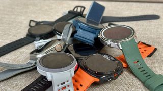 A pile of watches on a chair: The Garmin Fenix 8, Samsung Galaxy Watch Ultra, COROS VERTIX 2S, COROS PACE Pro, Samsung Galaxy Watch 7, Polar Vantage M3, and OnePlus Watch 2R