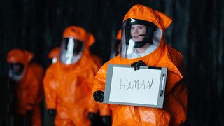 A scene from the movie Arrival, one of the best new movies on Paramount Plus, in which Amy Adam&#039;s character, Louise Banks, is wearing an orange hazmat suit and holding an orange sign that says human