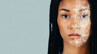 A close-up photo of a woman with long dark hair looking at the camera as her face is scanned by a facial recognition system