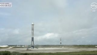 two black and white rocket boosters sit on a concrete pad under a cloudy gray sky.