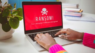 A laptop with a red screen with a white skull on it with the message: &quot;RANSOMWARE. All your files are encrypted.&quot;