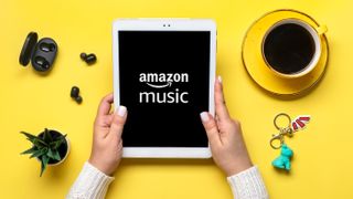 Woman holding tablet with Amazon Music app onscreen with yellow table surface in background