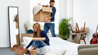 A woman with blonde hair unpacks boxes while sat on a mattress placed on the floor