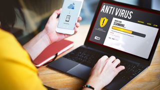 Woman holding a smartphone and installing an antivirus on her laptop