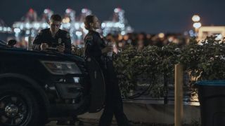 Troian Bellisario as Traci Harmon and Brandon Larracuente as Alex Diaz lean on the hood of their police truck with a nigh time cityscape in the background in On Call