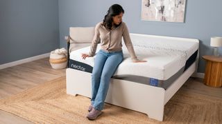 A woman with black hair sit on the Nectar Luxe memory foam mattress on a white bed frame