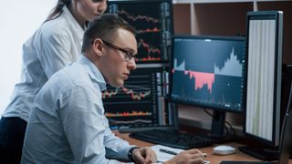 Team of stockbrokers are having a conversation in a office with multiple display screens