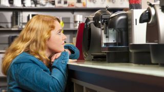 una mujer mirando una cafetera en la estantería de una tienda