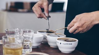 Person skimming grounds off bowls of coffee for cupping