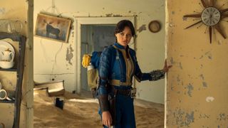 Ella Purnell as Lucy wearing a blue and yellow suit looking around a derelict house in Fallout.