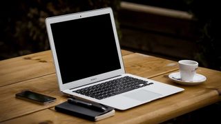 A laptop on a table, with a notepad and smartphone beside it.