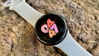 The Google Pixel Watch 3 sitting on a rock with the Index Bold watch face