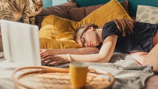 A college student falls asleep in front of her laptop on the couch while studying