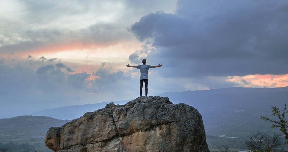 A person on the top of a rock at sunset