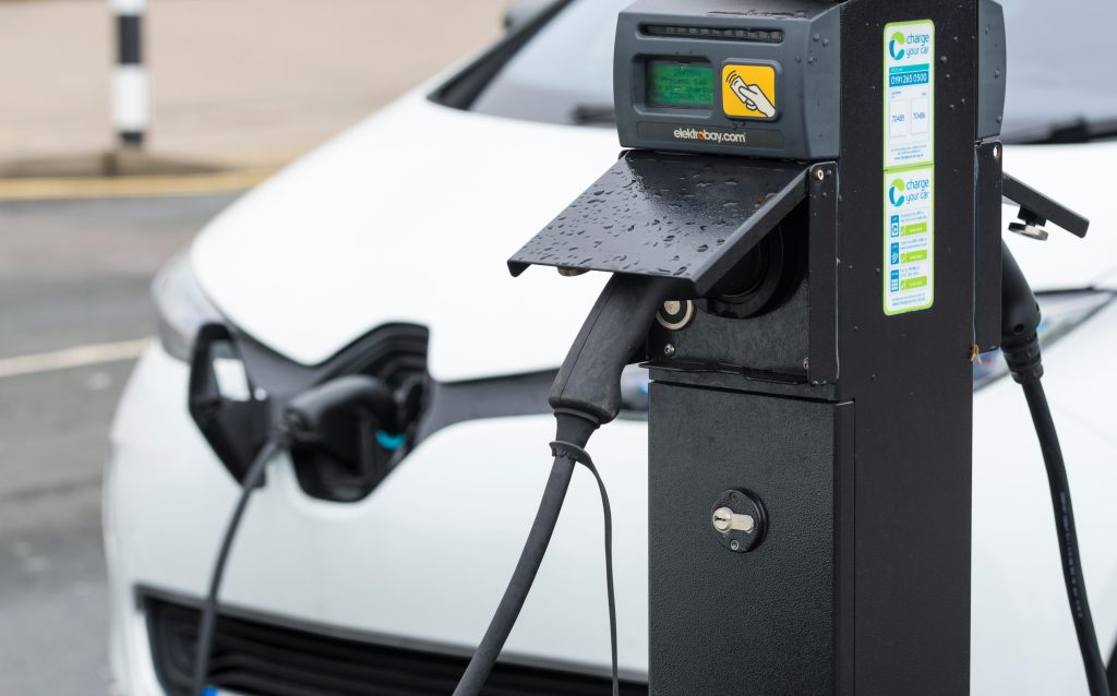 Photo: EV charging point with a small electric car plugged in while charging its batteries in Brighton, East Sussex, England, UK. Credit: Geoff Smith / Alamy Stock Photo 