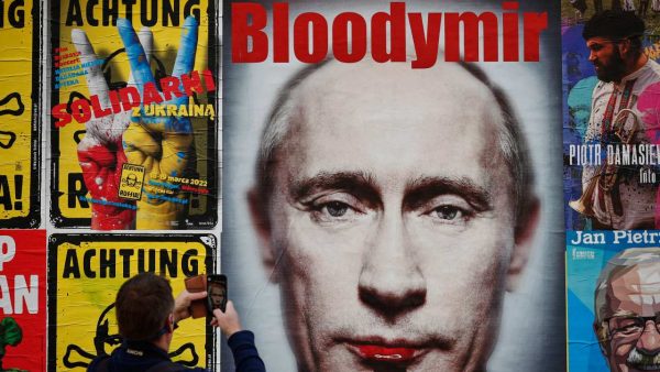 Photo: A man is seen taking a photo with his mobile phone of a poster with a portrait of Russian president Vladimir Putin in Warsaw, Poland on 23 March, 2022. Credit: STR/NurPhoto