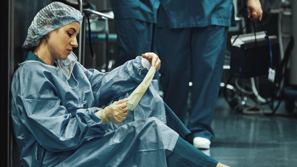 Photo: Tired doctor sitting after surgery in the hospital corridor. Great burden on doctors and medicine. Rest after work. Epidemic, lack of medical Credit: Georgiy Datsenko / Alamy Stock Photo