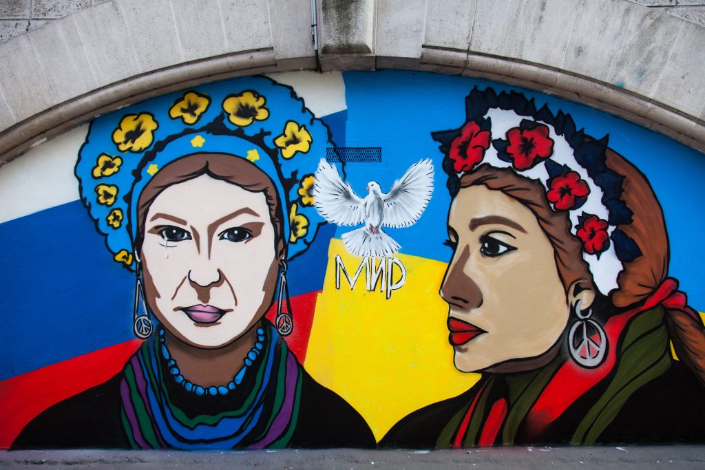 Photo: Street-art painting by the artist Djoulay La Papaye, in the streets of the 13th arrondissement of Paris, depicting two women wearing Slavic crowns made of flowers, one in the colors of the Ukrainian flag, the other in the colors of the Russian flag. On the left, the Ukrainian woman sheds a tear and wears earrings with the Peace and Love symbol. On the right, the Russian woman, who is looking at the Ukrainian woman, is wearing a big earring with the Peace and Love symbol. Between her, a white dove and a word in Cyrillic. Behind them, the Russian and Ukrainian flags. France, Paris, 2022-03-05. Credit: Maeva Destombes / Hans Lucas.