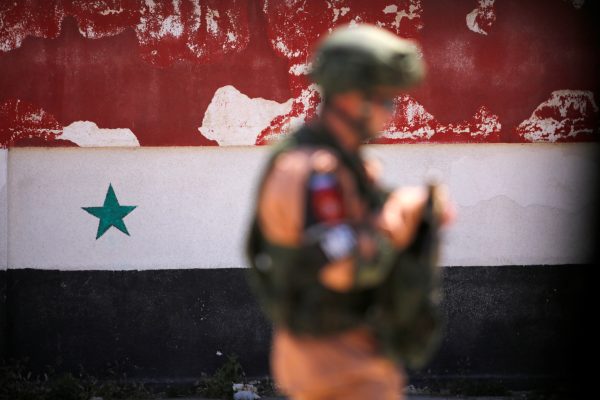 Photo: A Russian soldier stands guard near a Syrian national flag drawn on the wall as rebel fighters and their families evacuate the besieged Waer district in the central Syrian city of Homs, after an agreement reached between rebels and Syria's army, Syria May 21, 2017. Credit: REUTERS/Omar Sanadiki