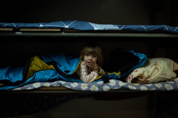 Photo: A Ukrainian child sleeps on a bunk bed with a blanket of blue and yellow, the colors of the Ukrainian flag. Credit: Elena Titus via https://war.ukraine.ua/wpcontent/uploads/2024/02/Tita_Elena_06.jpg