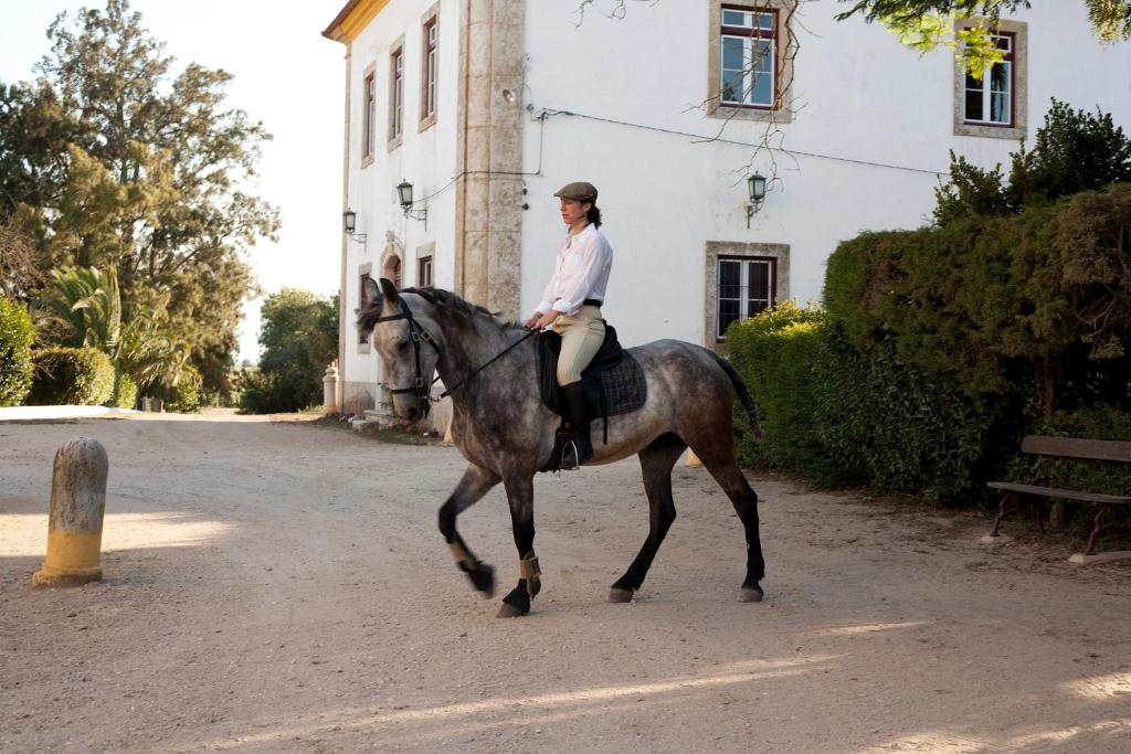 una mujer montando un caballo delante de un edificio en Quinta dos Álamos Agroturismo, en Golegã