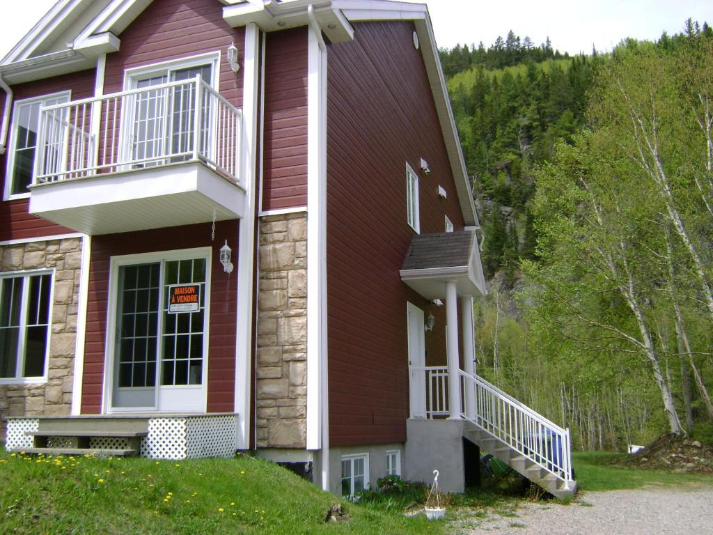 una casa roja con un balcón en el lateral. en Entre roc et montagne, en L'Anse-Saint-Jean