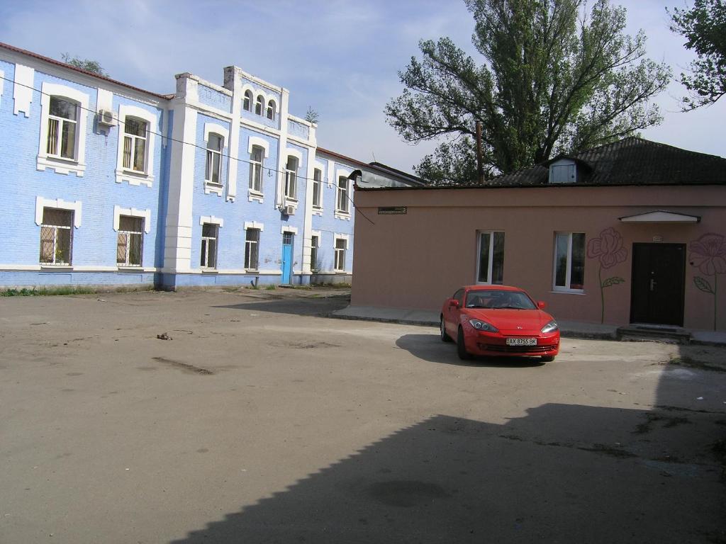 ein rotes Auto, das vor einem Gebäude parkt in der Unterkunft Hostel Raiduzhny in Kharkov