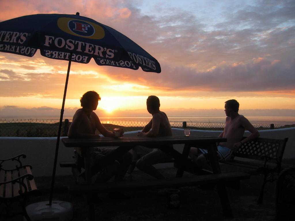 trois hommes assis à une table sous un parapluie dans l'établissement Longbeach- Adults Only, à Newquay