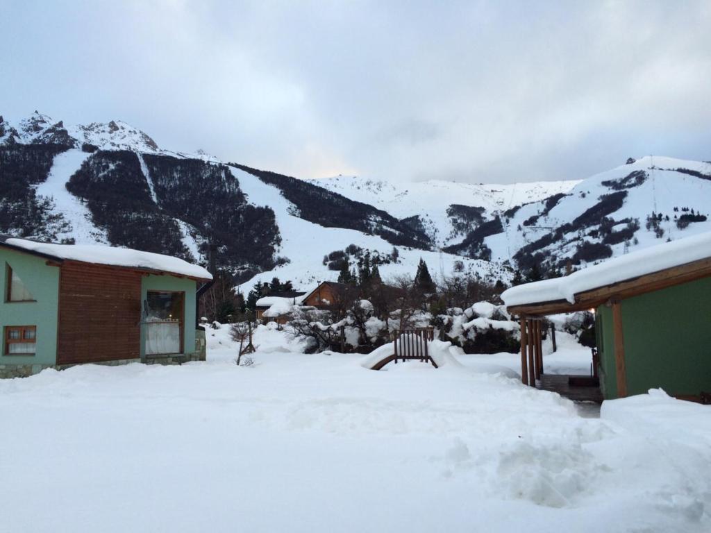 una casa cubierta de nieve con montañas en el fondo en Cabañas Ruca Carel, en San Carlos de Bariloche