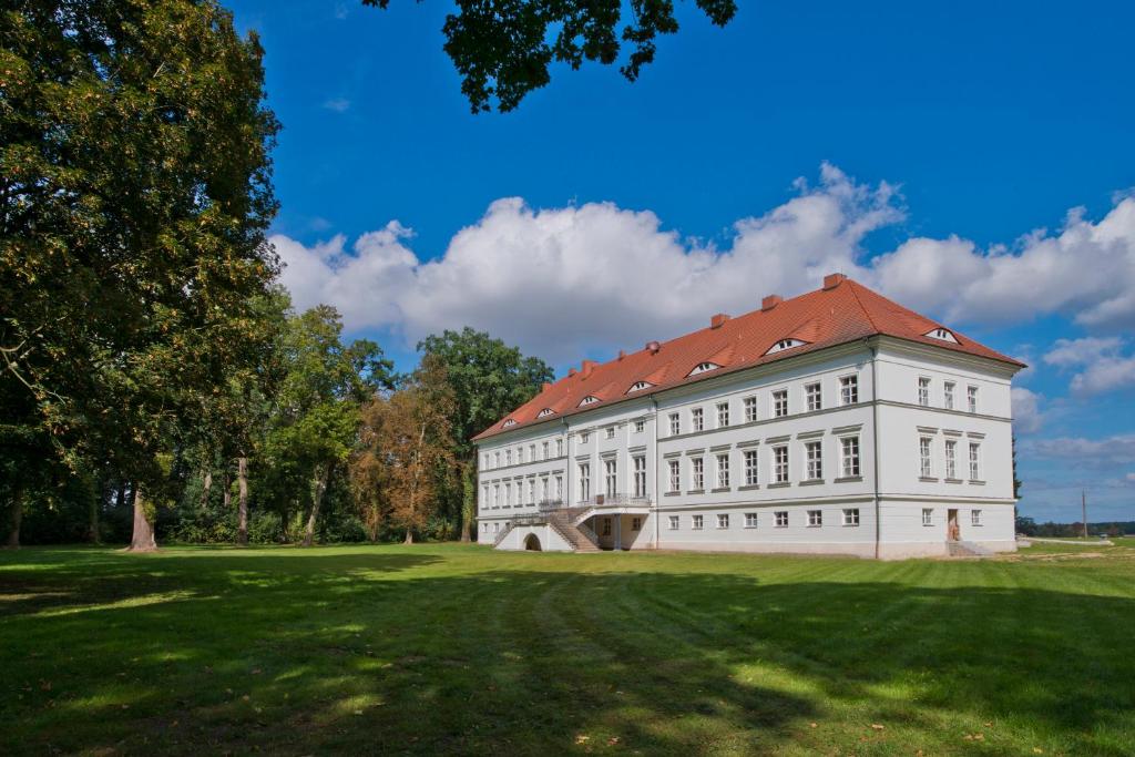 een wit gebouw met een rood dak op een groen veld bij Schloss Retzow Apartments in Retzow