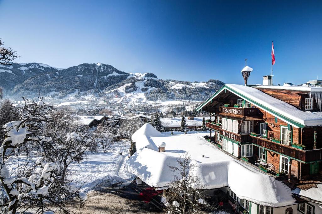 budynek pokryty śniegiem z górami w tle w obiekcie Relais & Châteaux Hotel Tennerhof w mieście Kitzbühel