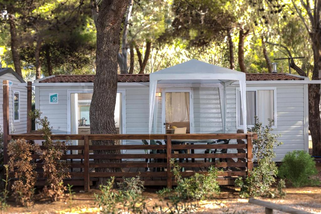 uma cabana branca com uma árvore e uma cerca em Giannella Camping em Orbetello