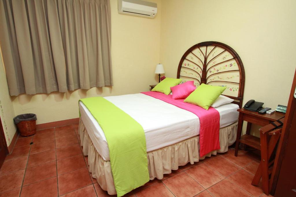 een slaapkamer met een bed met groene en roze kussens bij Hotel Colibri in Managua