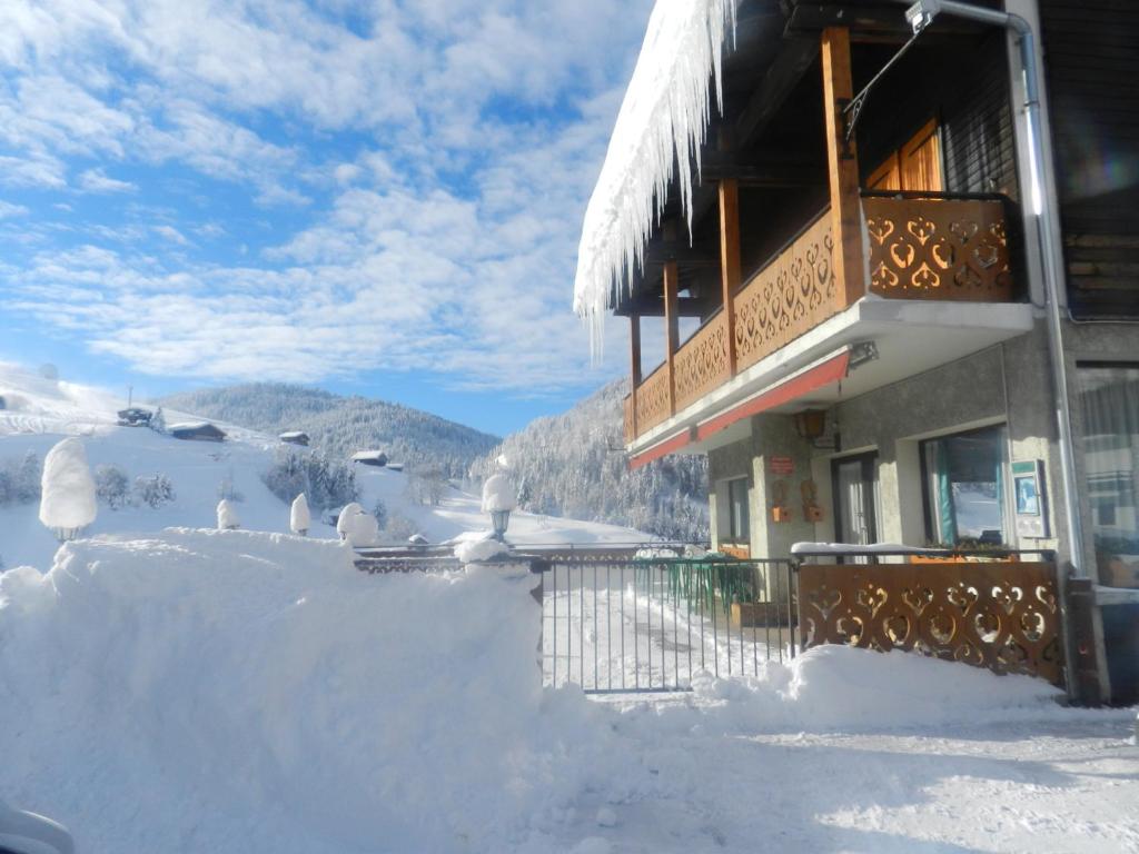 uma casa coberta de neve ao lado de uma cerca em Chalet-Hôtel du Borderan em La Clusaz