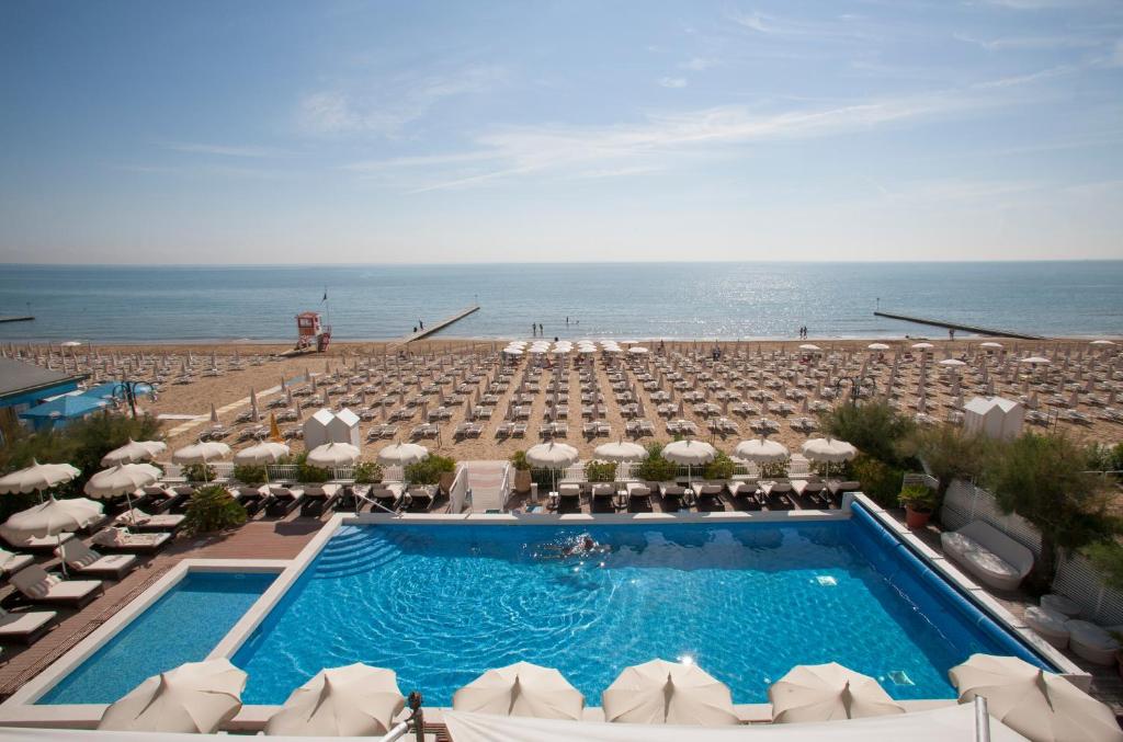 uma piscina com guarda-sóis e cadeiras e o oceano em Hotel Delle Nazioni em Lido di Jesolo