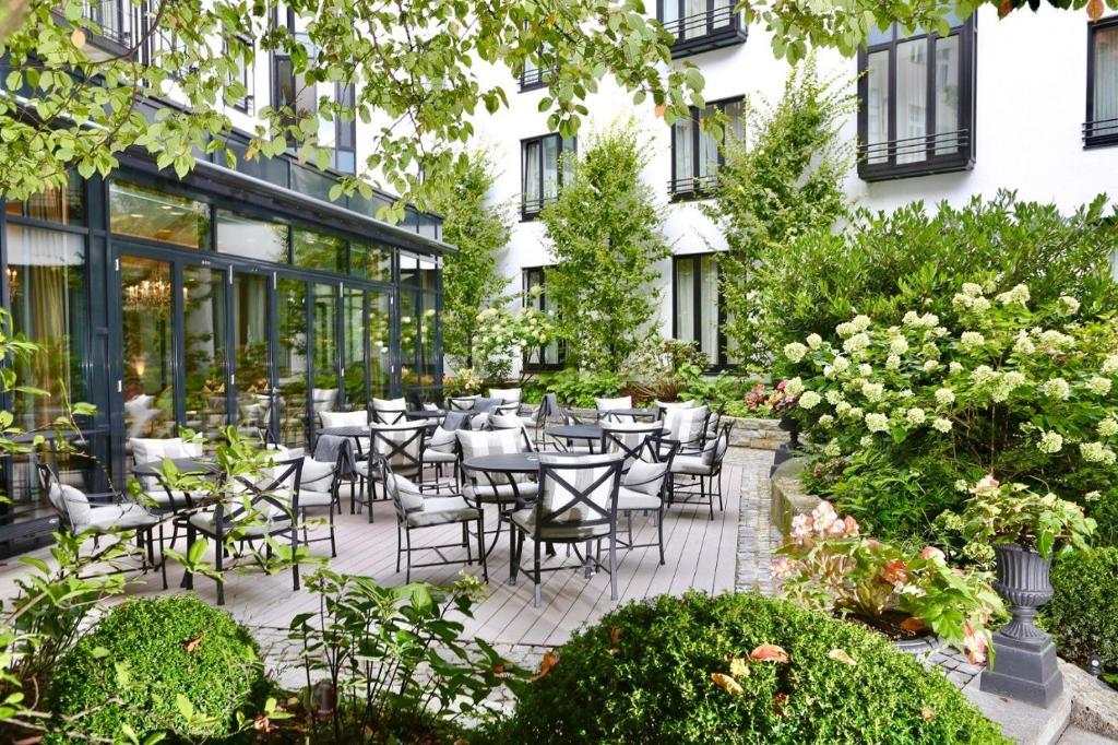 um pátio exterior com mesas, cadeiras e flores em Hotel München Palace em Munique