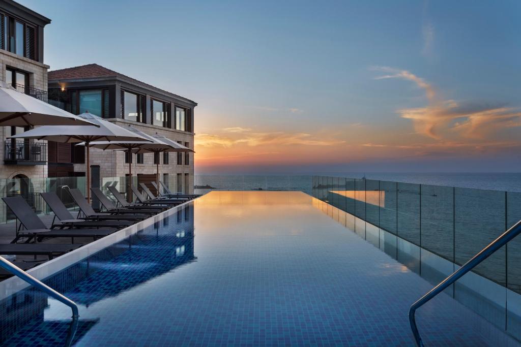 una piscina con sillas y el océano al atardecer en The Setai Tel Aviv, a Member of the leading hotels of the world, en Tel Aviv