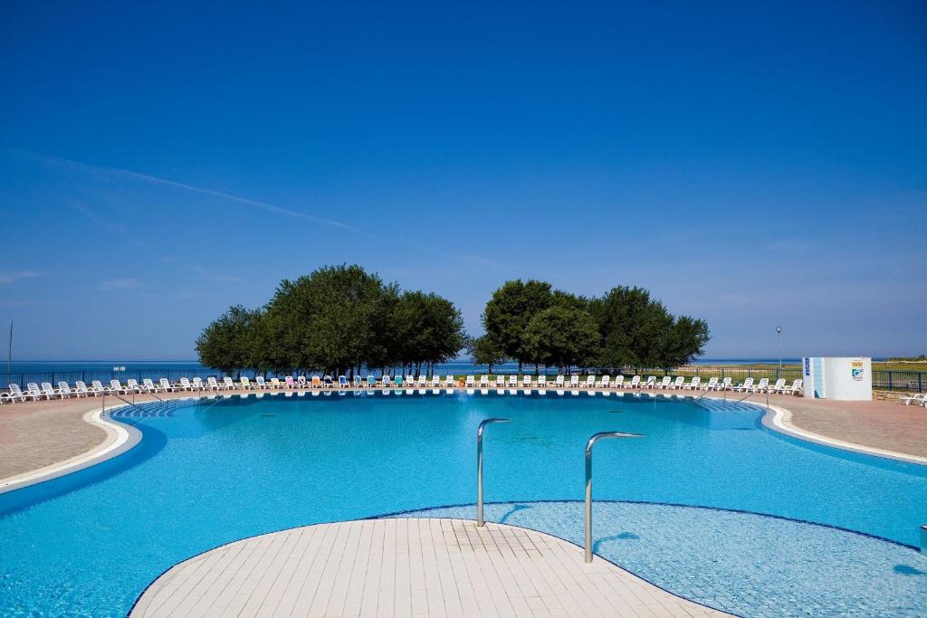 een zwembad met stoelen en blauw water bij Apartments Polynesia Plava Laguna in Umag