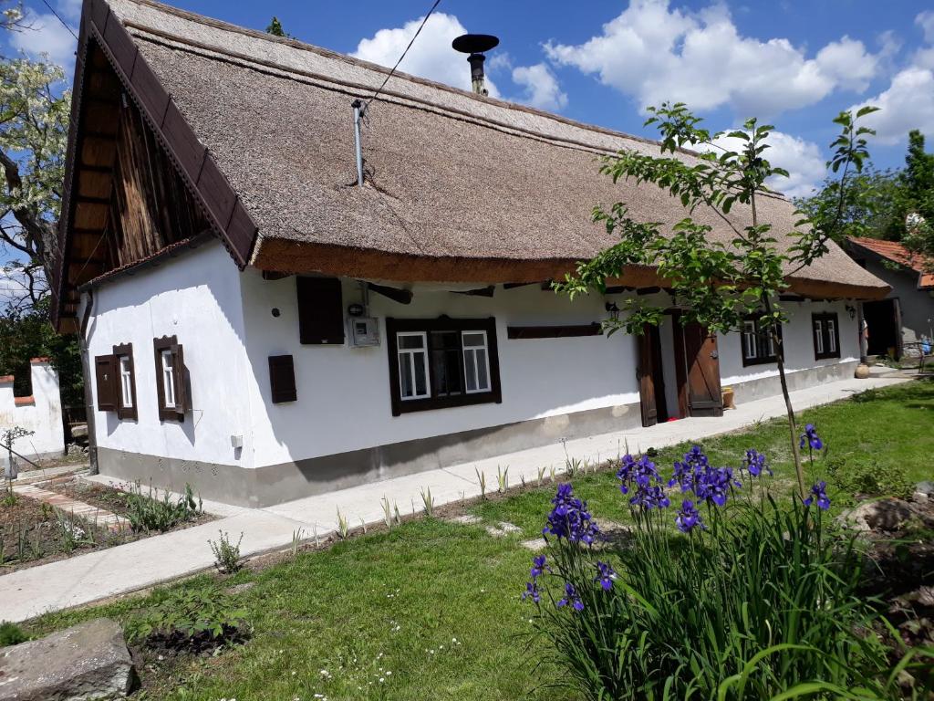 um chalé branco com telhado de palha e flores roxas em Forrás em Egerszólát