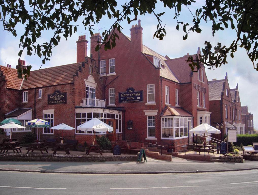 um grande edifício de tijolos com mesas e guarda-sóis em frente em Grosvenor Hotel em Robin Hood's Bay