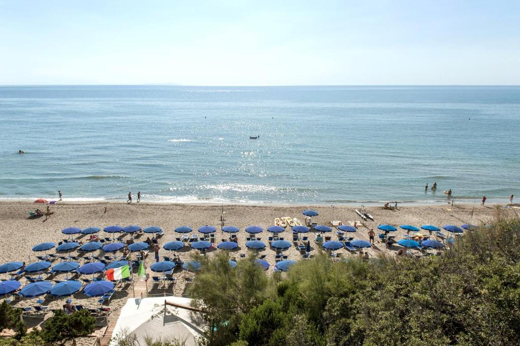 plaża z wieloma niebieskimi parasolami i oceanem w obiekcie Hotel Villa Lo Scoglietto w mieście San Vincenzo