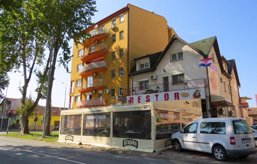 een witte auto geparkeerd voor een geel gebouw bij Domin Osijek in Osijek