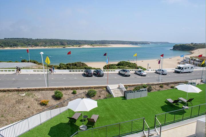 a lawn with umbrellas and a parking lot with a beach at Cerca da Vitoria 3 Milfontes in Vila Nova de Milfontes