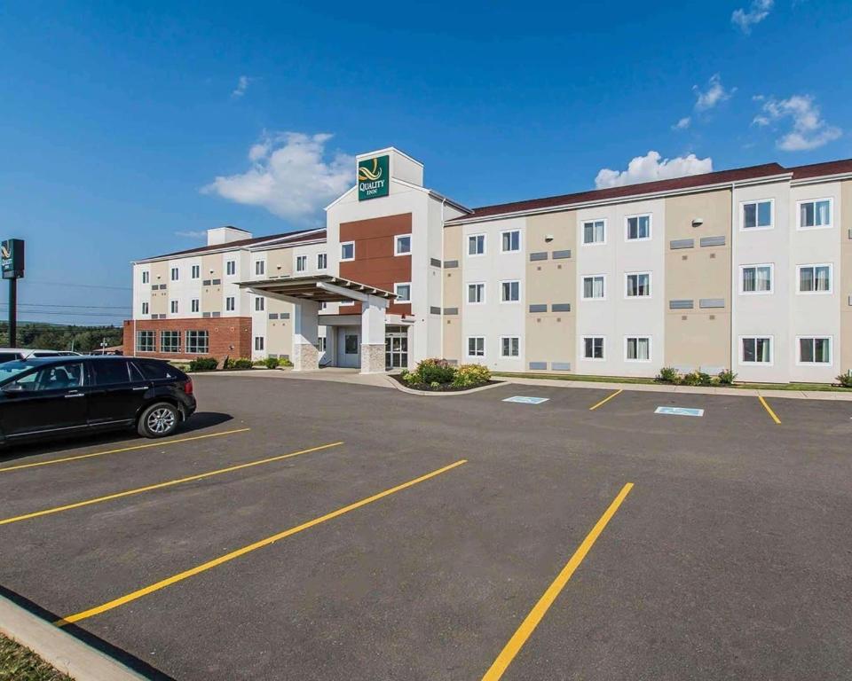 un grand bâtiment avec une voiture garée dans un parking dans l'établissement Quality Inn, à Moncton