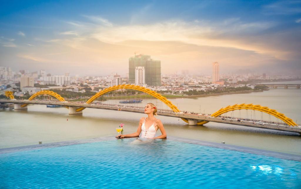 una mujer sentada en una piscina infinita con un puente en Val Soleil Hotel, en Da Nang