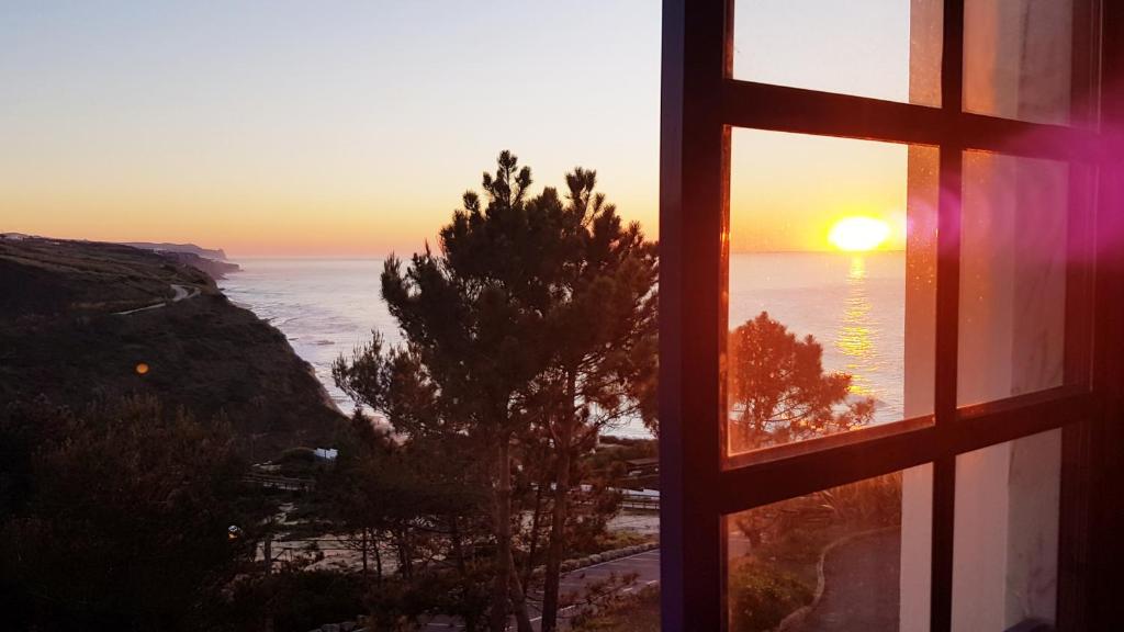 uma janela com vista para o oceano com o pôr-do-sol em Magoito Sea View Apartment em Lisboa