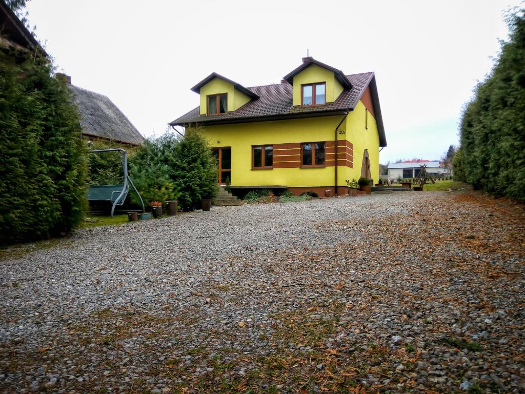 a yellow house with a black roof on a gravel road at Pokoje na Wiejskiej in Nałęczów