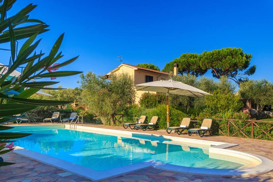 einem Pool mit Stühlen und einem Sonnenschirm neben einem Haus in der Unterkunft Agriturismo - B&B L'Acquacotta in Castiglione della Pescaia