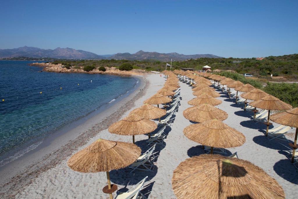 een rij rieten parasols op een strand bij Residence Baia Salinedda in San Teodoro